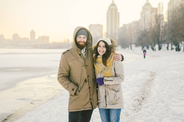 Theme love and date on nature. A young Caucasian heterosexual couple guy and girl walk in the winter along a frozen lake in winter. Bearded Man Hugging Woman. Valentine's day holiday. - Photo, Image