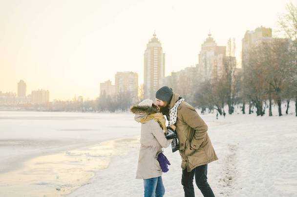 Theme love and date on nature. Young Caucasian heterosexual couple boy and girl kiss hugging warm scarf in winter near a frozen lake in winter. Bearded Man Hugging Woman. Valentine's day holiday. - Photo, Image