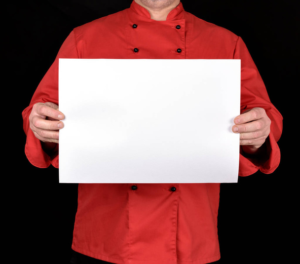 chef in red uniform holding a blank white paper sheet on a black background, copy space - Фото, изображение