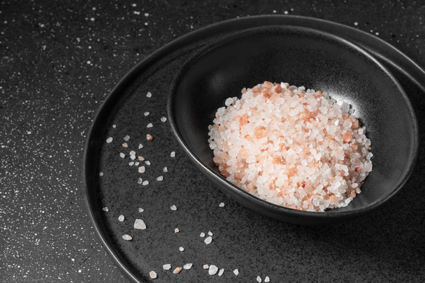 Pink sea salt in a black dish on a dark background - Foto, Imagen
