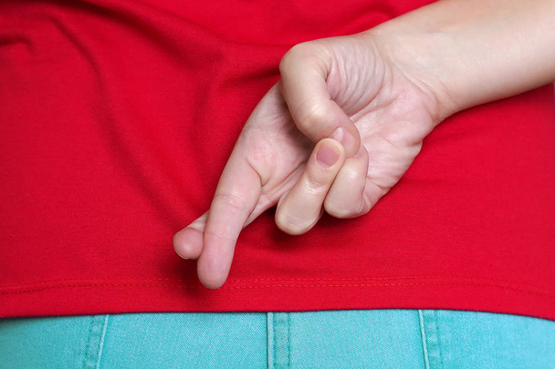 Close-up of young female holding finger crossed behind her back. - Photo, Image