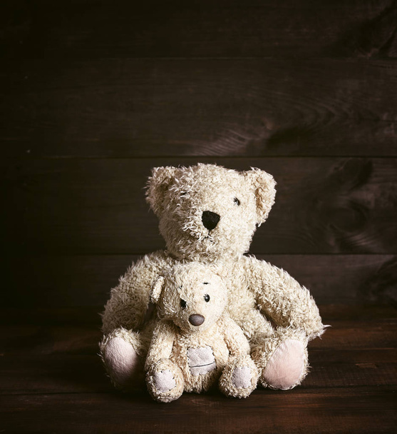 two old brown soft teddy bears are sitting on a wooden surface, vintage toning - Foto, afbeelding