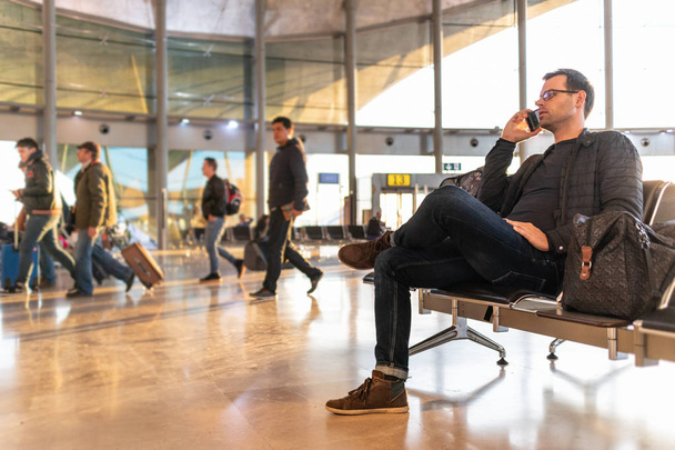 Hombre viajero hablando en su teléfono celular mientras espera para abordar un avión a las puertas de salida en la terminal del aeropuerto
. - Foto, Imagen
