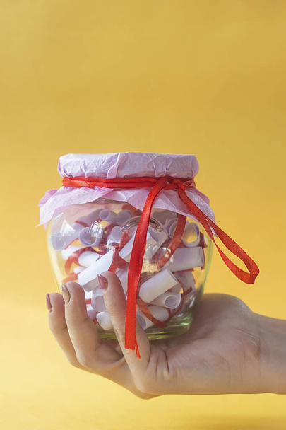 Concept de Saint-Valentin. Femme tenant pot en verre rempli de papiers roulés désirs, souhaits ou rêves sur jaune
 - Photo, image