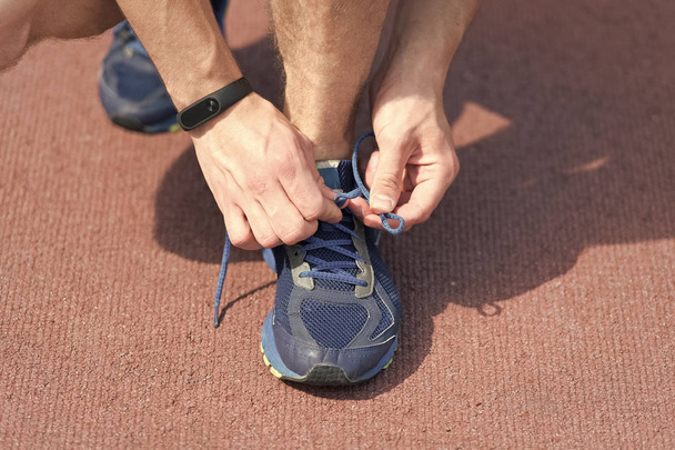 Hands tying shoelaces on sneaker, running surface background. Hands of sportsman with pedometer tying shoelaces on sporty sneaker. Running equipment concept. Shoelaces tying by male hands - Photo, image