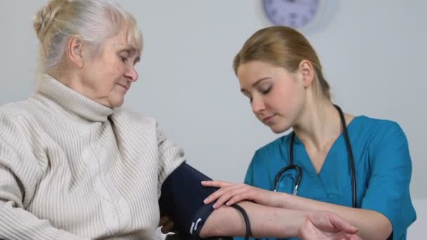 Jeune infirmière mesurant la pression artérielle féminine âgée handicapée et prenant des dossiers
 - Séquence, vidéo