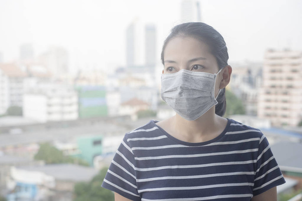 Mulher usando máscara facial de N95 por causa da poluição do ar na cidade tem partículas ou PM 2.5 com fundo de construção da cidade
 - Foto, Imagem
