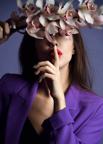 Beautiful girl with orchid flowers. Beauty model woman face on purple background  - Fotografie, Obrázek