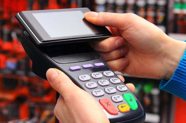 Mão de mulher que paga com leitor de cartão de crédito com telefone celular com tecnologia NFC, pagando sem dinheiro para compras ou conceito de produtos
 - Foto, Imagem