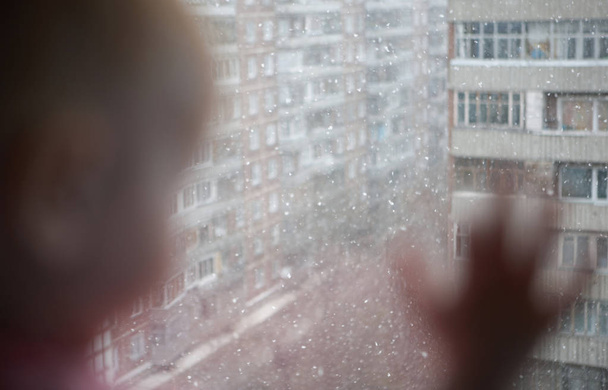 Ένα μικρό παιδί που κοιτάζει έξω από το παράθυρο του επάνω ορόφου του σπιτιού, το ακουμπά στο γυαλί - Φωτογραφία, εικόνα