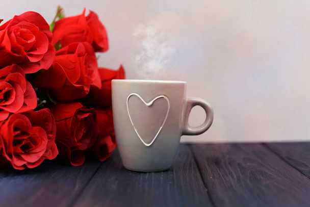 kopje koffie met een drankje met een hart op een houten achtergrond met rode bloemen voor het feest van St. Valentine's Day  - Foto, afbeelding