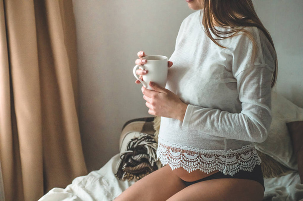 Приваблива вагітна жінка п'є чай на ліжку. Пити чай, дивлячись через вікно вдома. Останні місяці вагітності
. - Фото, зображення