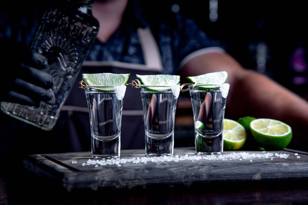 aperitivo con amigos en el bar, tres vasos de alcohol con lima y sal para decorar. Tequila shots, enfoque selectivo
 - Foto, Imagen