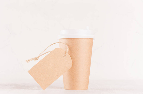 Coffee packing mockup -  craft brown paper cup with white cap and blank label closeup on white wood board, coffee shop interior. Modern elegant concept for branding identity, advertising, design. - 写真・画像