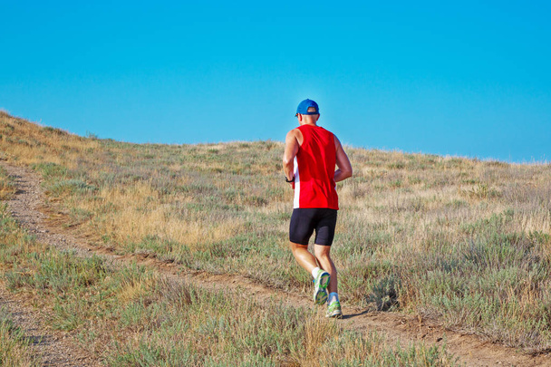 rear view of athletic runner running on a mountain trail on a blue sky background - Photo, Image