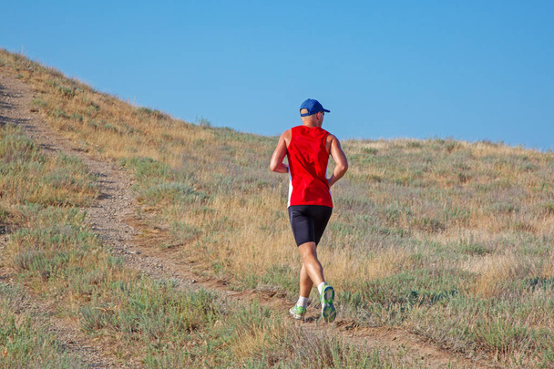 visão traseira do corredor atlético correndo em uma trilha de montanha em um fundo céu azul
 - Foto, Imagem