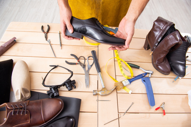 Молодой человек ремонтирует обувь в мастерской
  - Фото, изображение