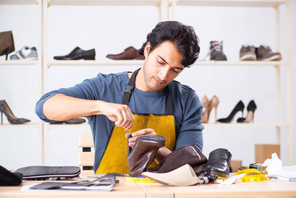 Молодой человек ремонтирует обувь в мастерской
  - Фото, изображение