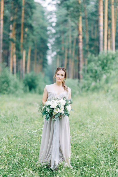 Boudoir photo shoot of the bride in the woods with a bouquet. Flying dress and beautiful girl in the Park. - Фото, изображение