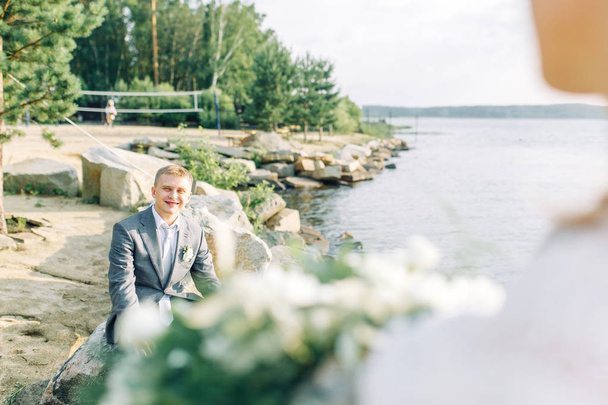 Groom in nature by the water. Gathering of a young man on the pier at sunset. - Photo, image