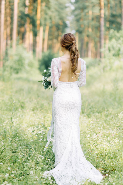 The bride in a wedding dress in nature with a bouquet. Boudoir photo shoot in pine lemu in the style of fine art. - Foto, Imagen