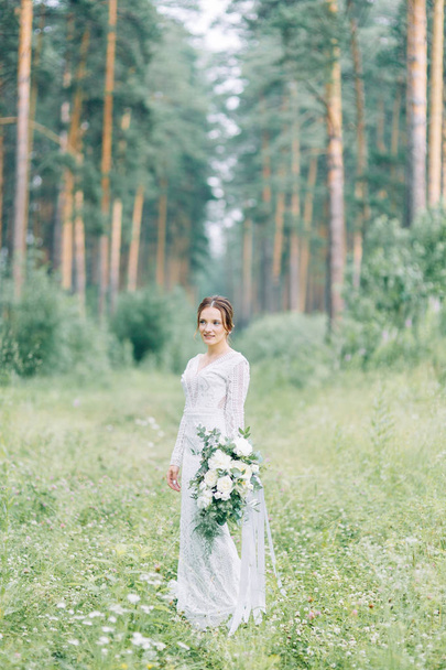 The bride in a wedding dress in nature with a bouquet. Boudoir photo shoot in pine lemu in the style of fine art. - Foto, Imagen