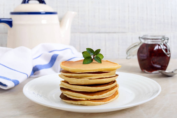 Heerlijke pannenkoeken met frambozen jam op een witte plaat op de keukentafel. Klassieke Amerikaanse zelfgemaakte ontbijt. - Foto, afbeelding