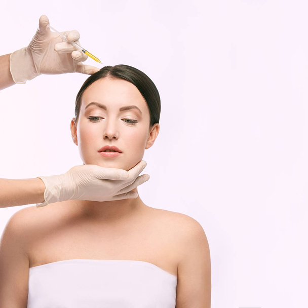 Face needle injection. Young woman cosmetology procedure. Doctor gloves. - 写真・画像