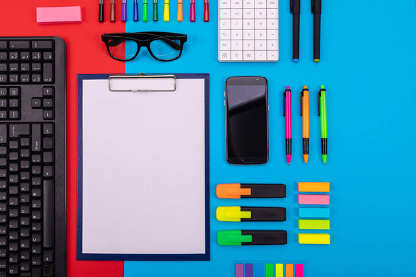 Composição de leigos planos de mesa de negócios com smartphone, área de transferência, adesivos e caneta em fundo azul e vermelho colorido
 - Foto, Imagem