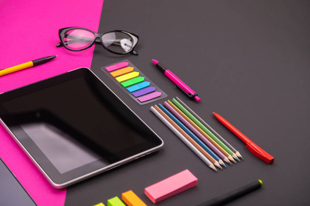 Picture of modern artspace with tablet, glasses, stationery and smartphone on pink and black background. Flat lay style - Photo, Image