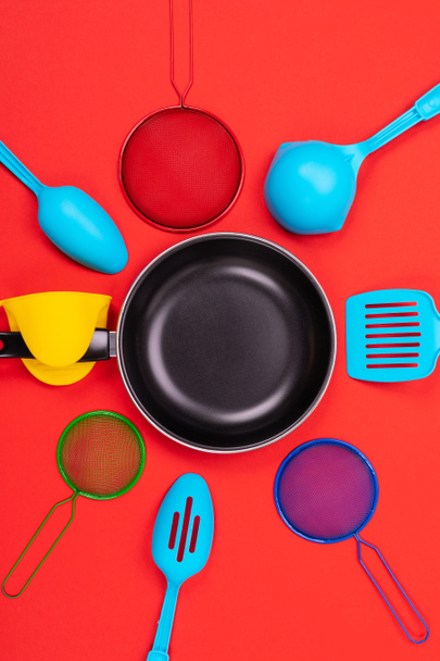 Sartén en el centro con utensilios de cocina alrededor aislados sobre fondo rojo
 - Foto, Imagen