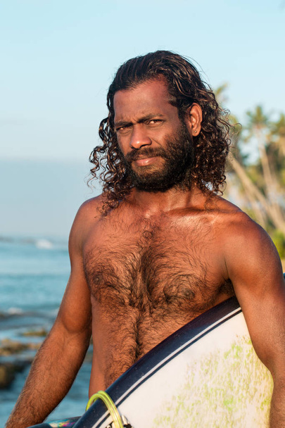 Сёрфер держит доску для серфинга на берегу Индийского океана
 - Фото, изображение