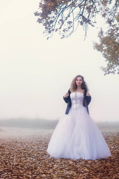 Beautiful bride near oak in the autumn foggy day - Foto, afbeelding