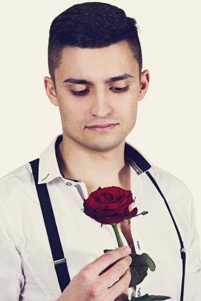 Ένας άντρας με κόκκινο τριαντάφυλλο στα χέρια. Ημέρα του Αγίου Βαλεντίνου - Φωτογραφία, εικόνα