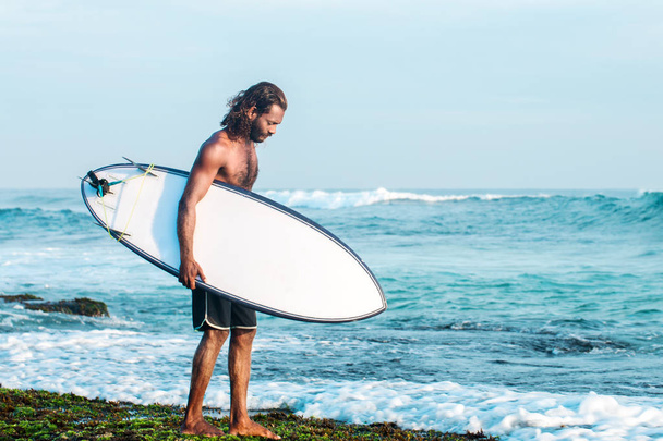 Sörfçü bir sörf tahtası Hint Okyanusu kıyısında tutuyor - Fotoğraf, Görsel