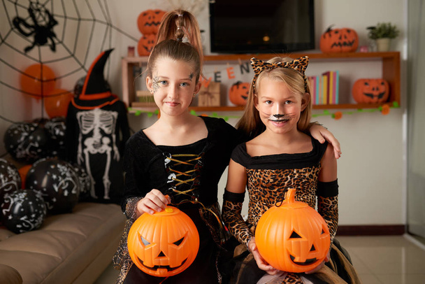 Retrato de lindas niñas caucásicas con caras pintadas sonriendo a la cámara mientras posan en disfraces de Halloween con calabazas
 - Foto, imagen