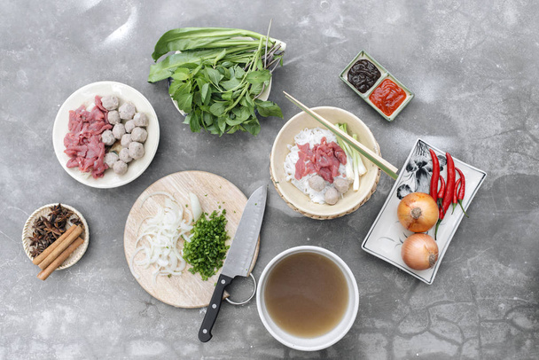 Παραδοσιακό βιετναμέζικο σούπα Pho bo με βότανα, κρέατα, noodles ρυζιού, ζωμό. Pho bo σε μπολ με chopsticks, κουτάλι. Χώρο για το κείμενο. Το Top view. Ασιατική σούπα Pho bo στο φόντο ξύλινο τραπέζι. Βιετναμέζικα-σούπα - Φωτογραφία, εικόνα