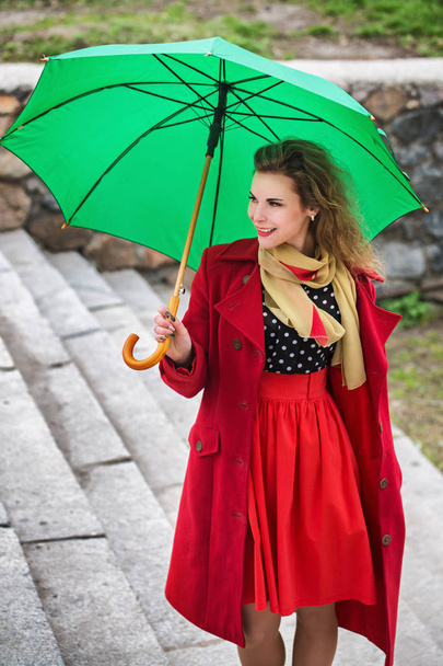 schöne Frau im roten Mantel hält einen grünen Regenschirm - Foto, Bild
