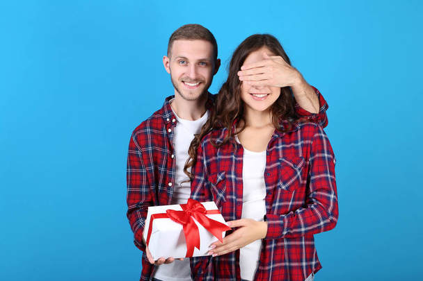 Beautiful young couple with gift box on blue background - Photo, image