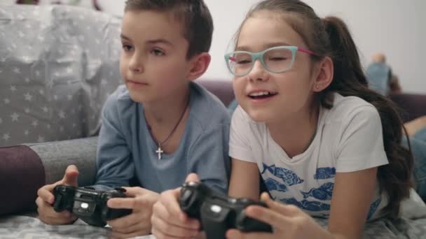 Children playing video games. Kids lying on sofa with controller in hands - Séquence, vidéo