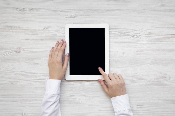 Vrouwelijke handen met behulp van Tablet PC op een witte houten ondergrond, top uitzicht. Van bovenaf leggen overhead, plat. - Foto, afbeelding