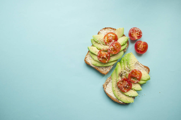 Plochou položit výborné toasty s plátky avokádem, rajčaty a sezamová semena na modrém podkladu s copyspace. - Fotografie, Obrázek