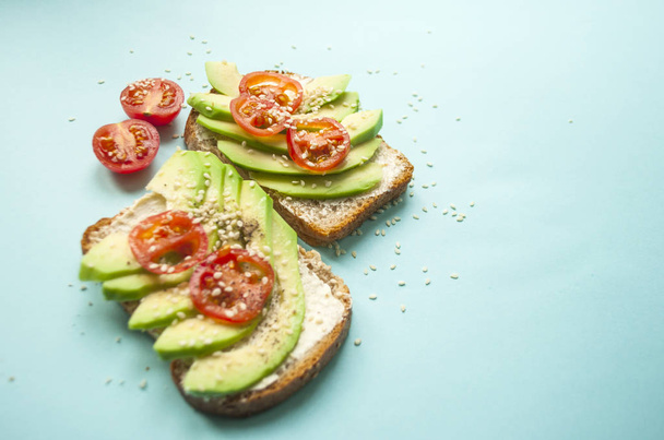 Close up of delicious toasts with sliced avocado, tomatoes and sesamum seeds on blue background with copyspace. Healthy food concept. - Valokuva, kuva