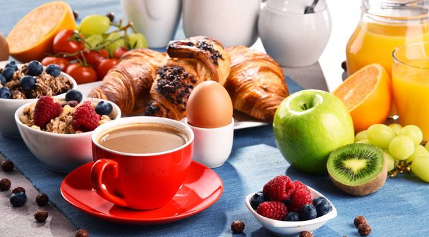 Aamiainen tarjoillaan kahvin, appelsiinimehun, croissanttien, munien, viljan ja hedelmien kera. Tasapainoinen ruokavalio. - Valokuva, kuva