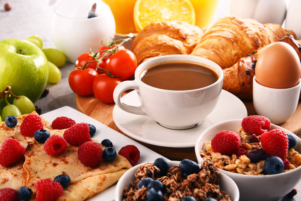 Aamiainen tarjoillaan kahvin, appelsiinimehun, croissanttien, munien, viljan ja hedelmien kera. Tasapainoinen ruokavalio. - Valokuva, kuva