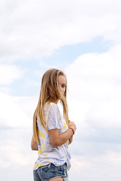 Long-haired young beautiful girl on a background of clouds - Photo, Image