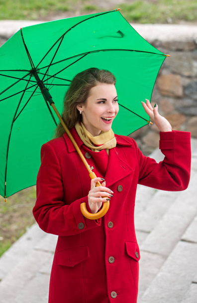 Όμορφη γυναίκα σε ένα κόκκινο παλτό κρατά μια πράσινη ομπρέλα - Φωτογραφία, εικόνα