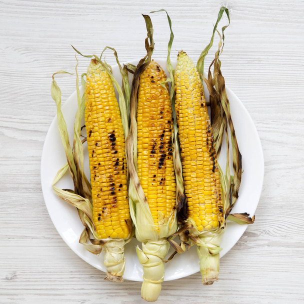 Grilled sweet corn on a white round plate over white wooden surface, top view. Summer vegan snack. Healthy diet. Close-up. - Zdjęcie, obraz