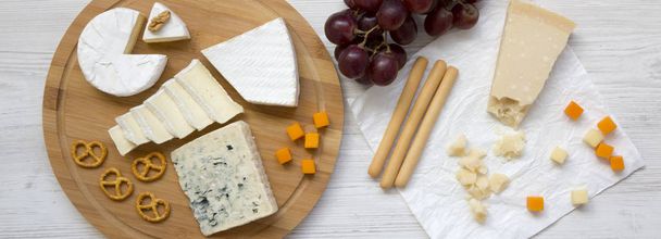 Tasting delicious cheese with grapes, walnuts, bread sticks and pretzels on wooden surface, overhead view. Food for wine. From above. Flat lay.  - Photo, Image