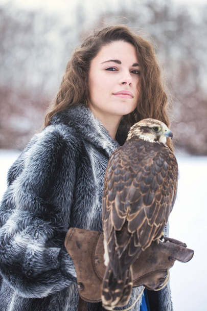 Beautiful woman holding a falcon on her hand in winter - Photo, Image